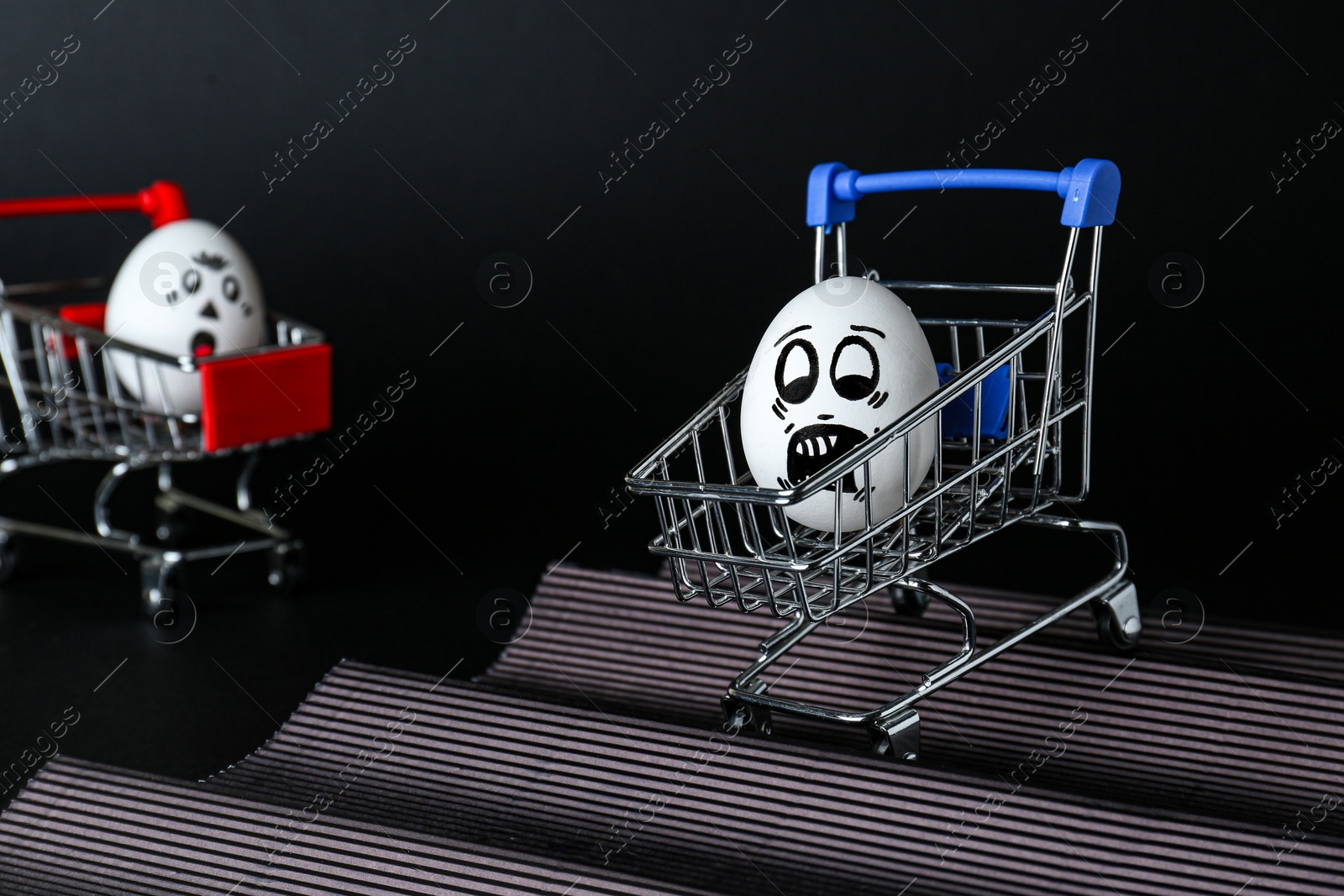 Photo of Egg with drawn scared face in shopping cart stunting on black background