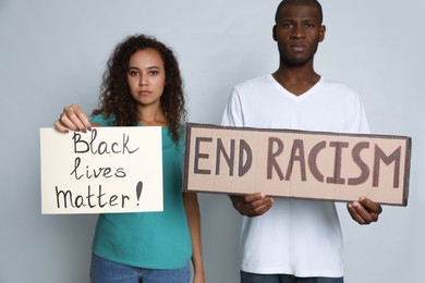 Photo of African American woman and man holding signs on grey background. Racism concept