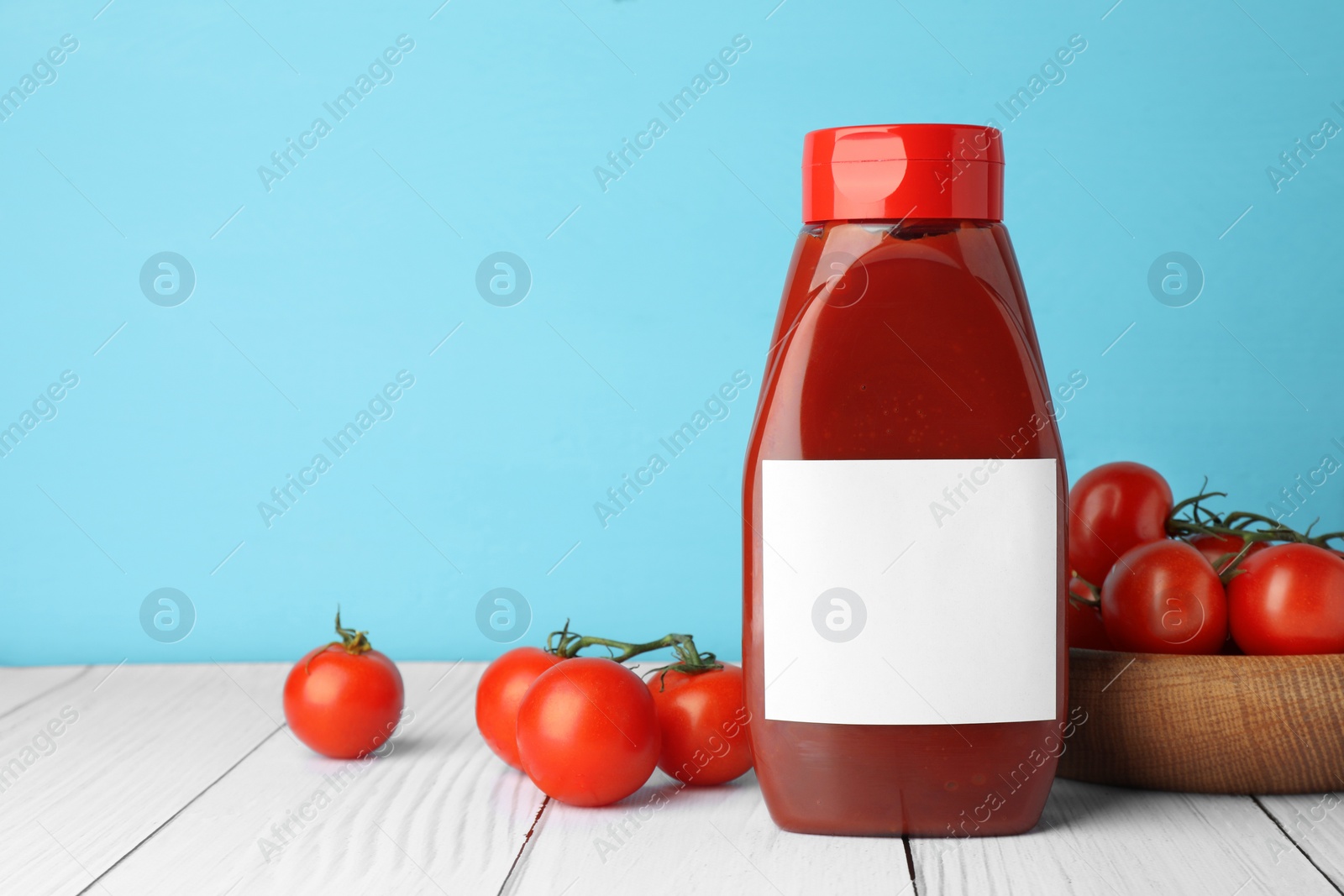 Photo of Bottle of tasty ketchup and tomatoes on white wooden table. Space for text