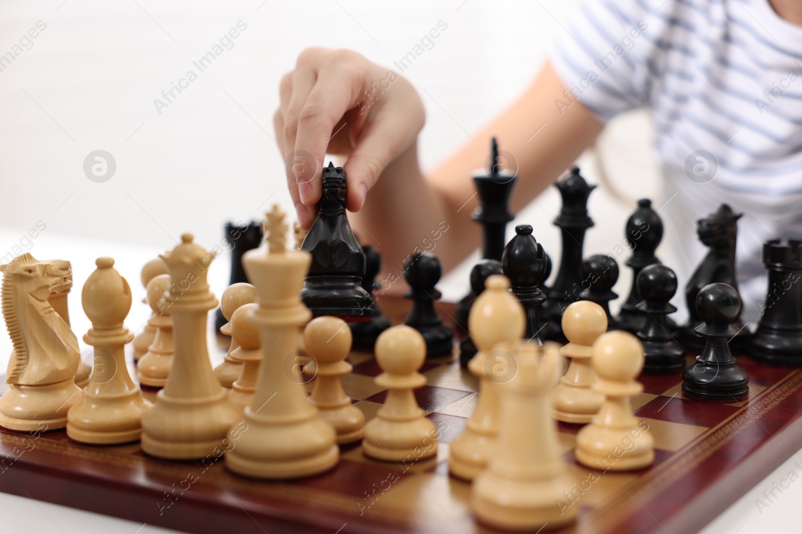 Photo of Little child playing chess at table indoors, closeup