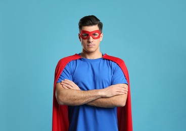 Man wearing superhero cape and mask on light blue background