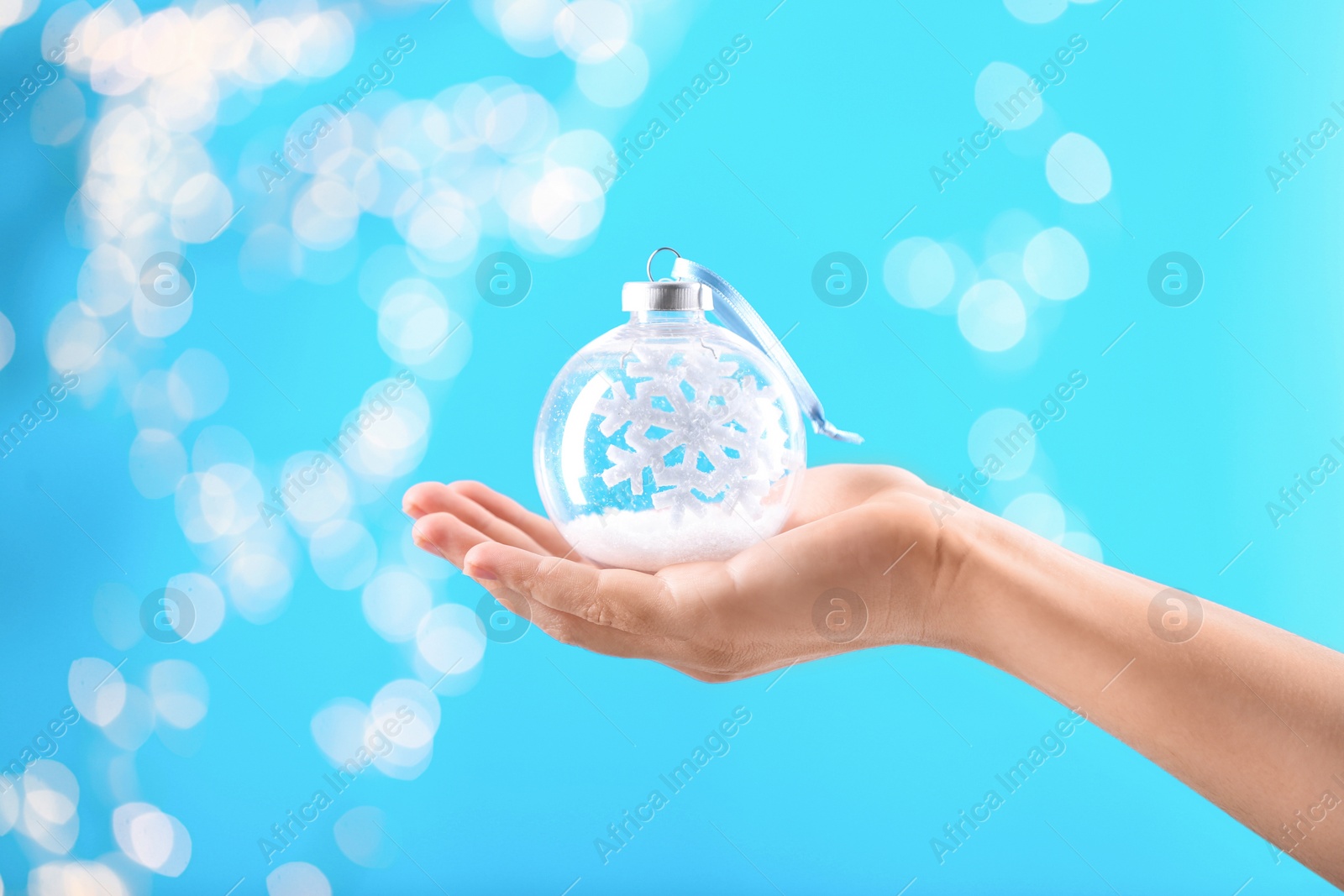 Photo of Woman holding decorative snow globe against blurred festive lights, closeup