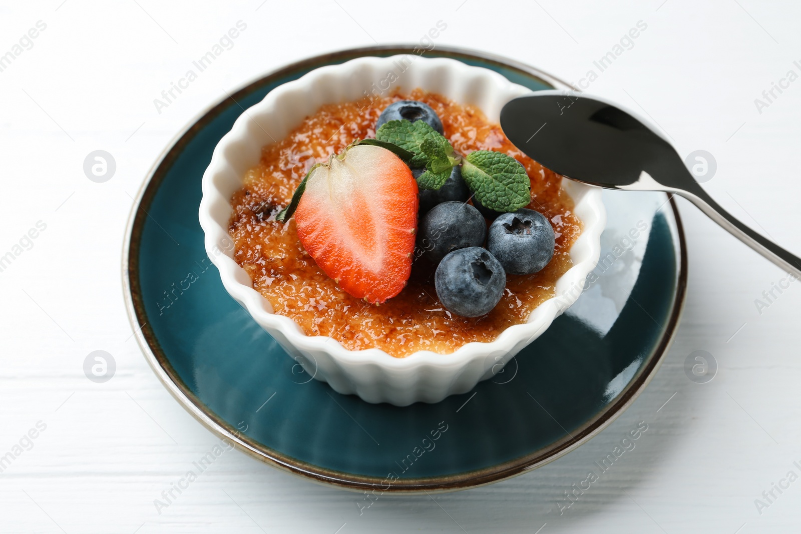 Photo of Delicious creme brulee with berries and mint in bowl on white wooden table, closeup