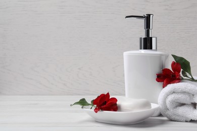 Photo of Dish with soap bar, dispenser and terry towel on white wooden table. Space for text