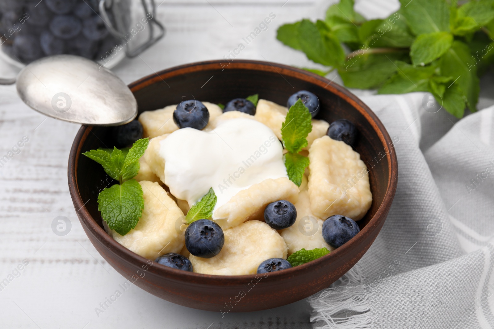 Photo of Bowl of tasty lazy dumplings with blueberries, sour cream and mint leaves on white wooden table