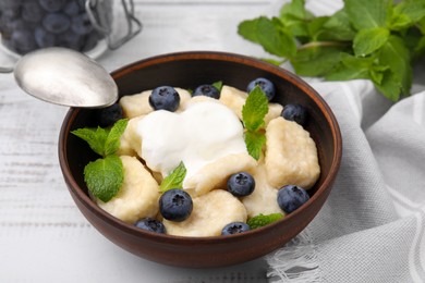 Photo of Bowl of tasty lazy dumplings with blueberries, sour cream and mint leaves on white wooden table