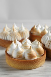 Many different tartlets with meringue on white wooden table, closeup. Tasty dessert