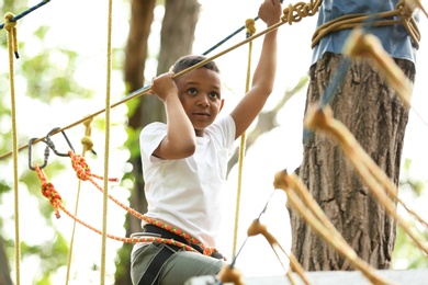 Photo of Little African-American boy climbing in adventure park. Summer camp