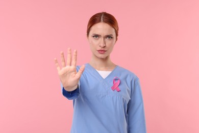 Photo of Mammologist with pink ribbon showing stop gesture on color background. Breast cancer awareness