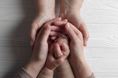 Photo of Family holding hands together at white wooden table, top view