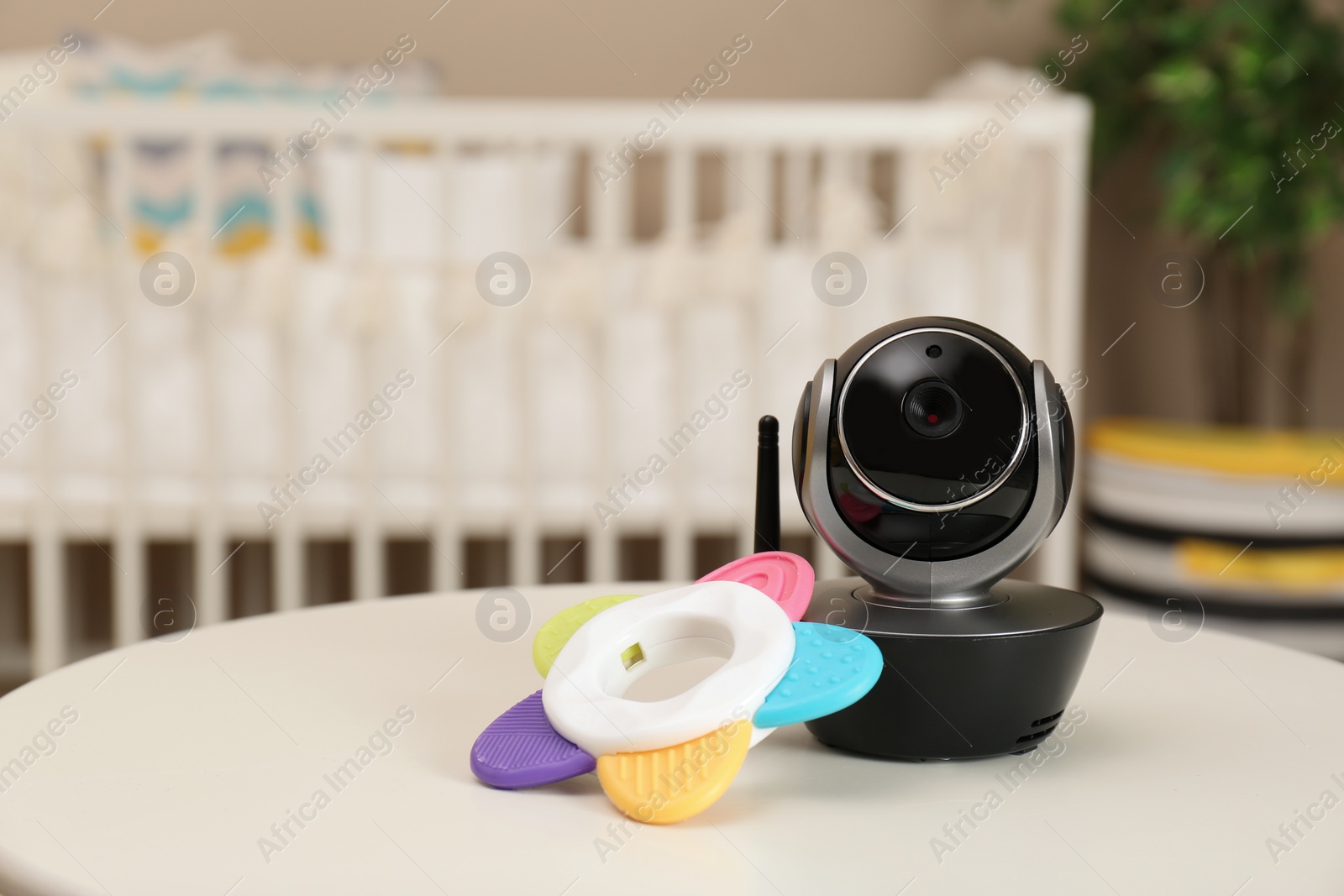 Photo of Modern CCTV security camera and teether on table in nursery. Space for text