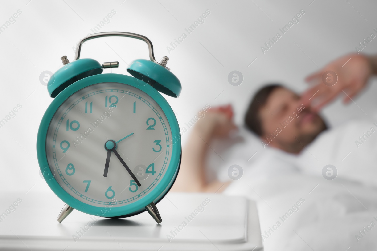 Photo of Sleepy man awaking at home in morning, focus on alarm clock. Space for text