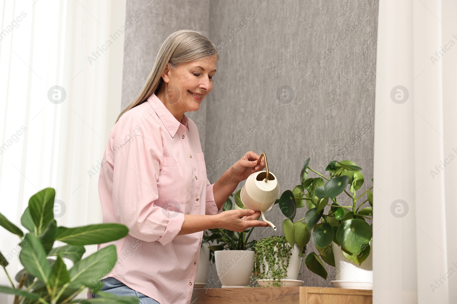 Photo of Happy housewife watering green houseplants at home