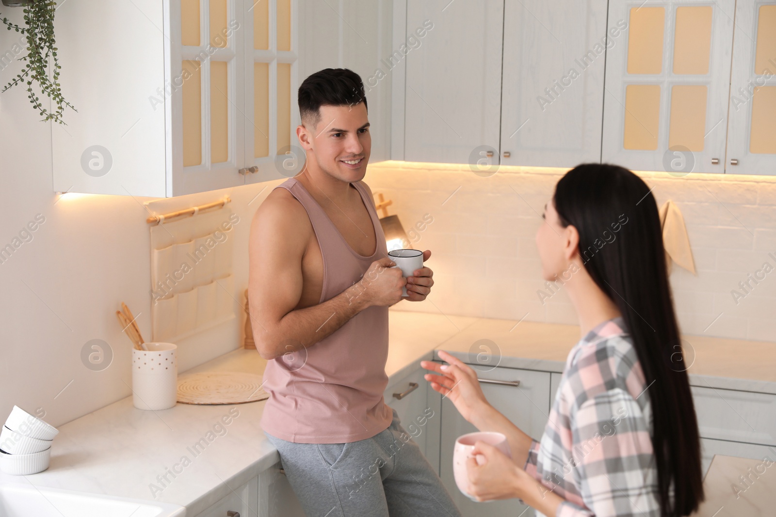 Photo of Happy couple wearing pyjamas with cups of coffee in kitchen