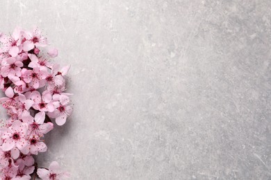 Photo of Sakura tree branch with beautiful pink blossoms on light stone table, flat lay. Space for text