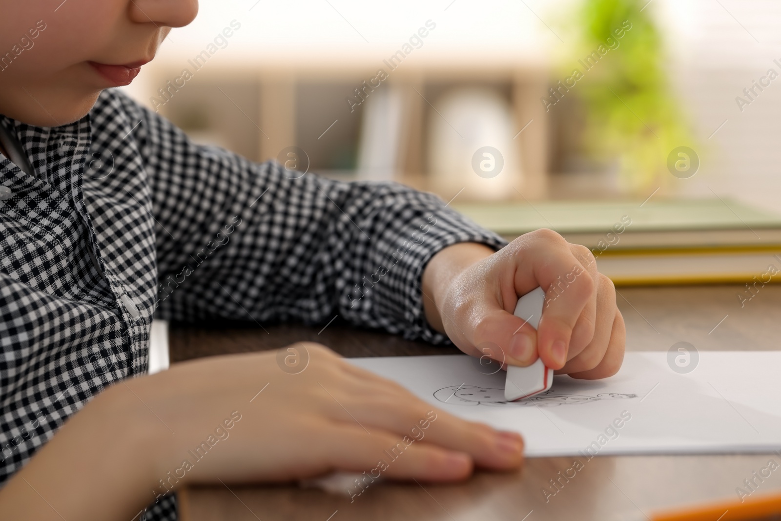 Photo of Little boy erasing mistake in his notebook at wooden desk indoors, closeup