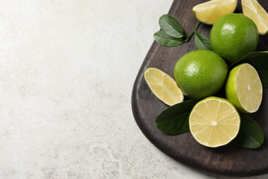 Fresh limes and green leaves on light table, top view. Space for text