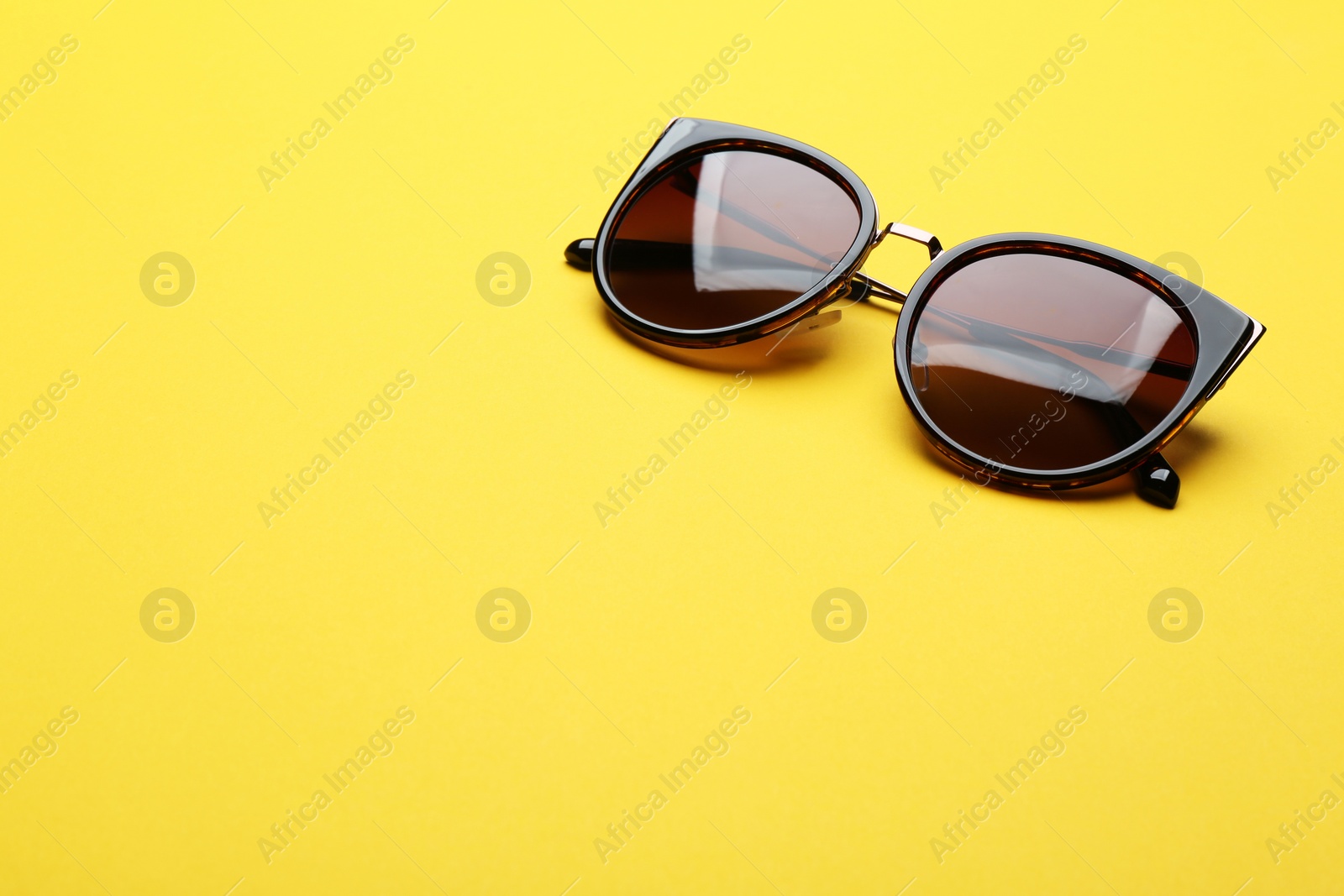 Photo of Stylish sunglasses on yellow background, space for text. Fashionable accessory