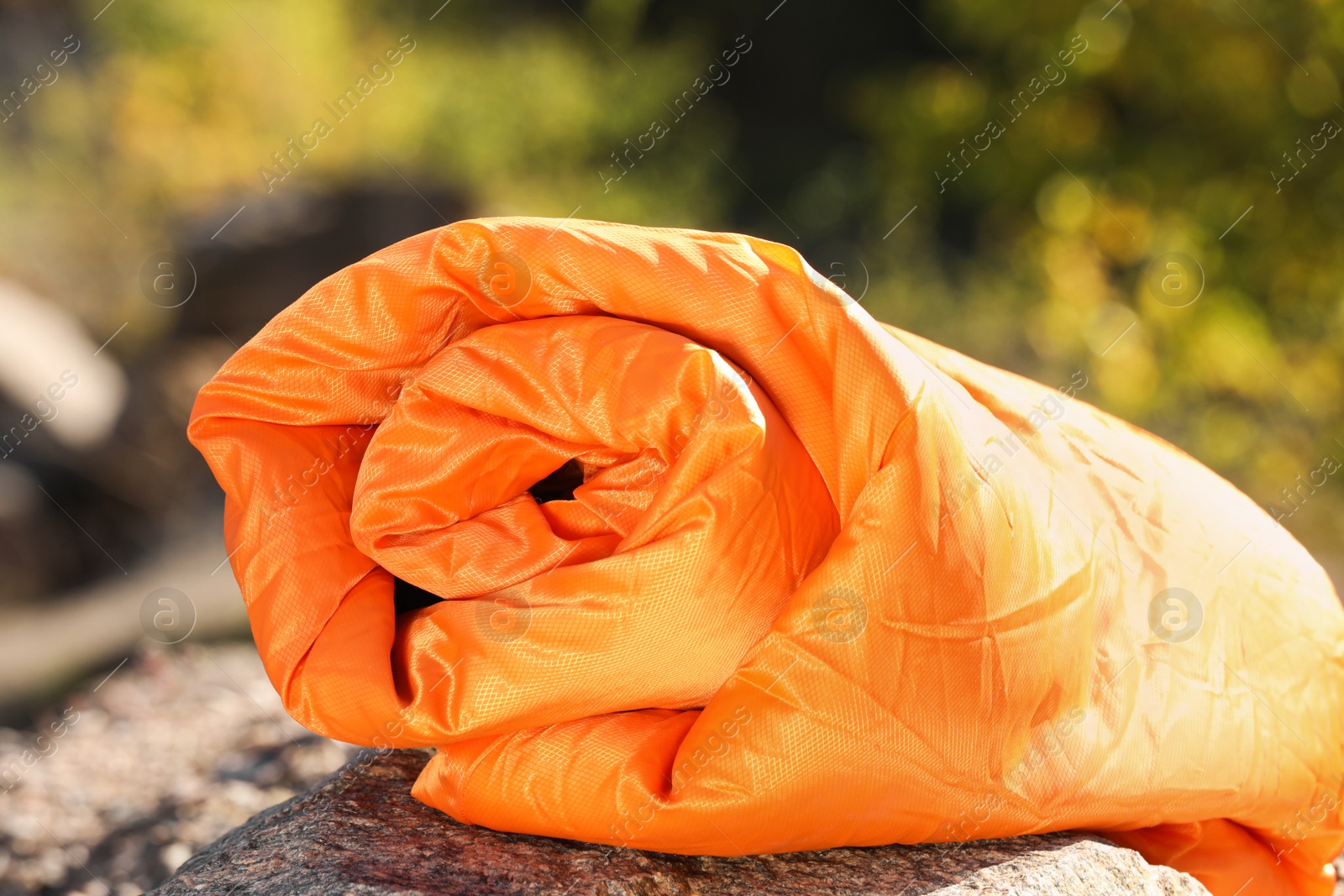 Photo of Orange sleeping bag on rock outdoors. Camping equipment