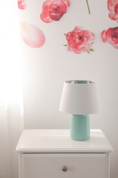 Photo of Lamp on nightstand near floral wall indoors. Interior design