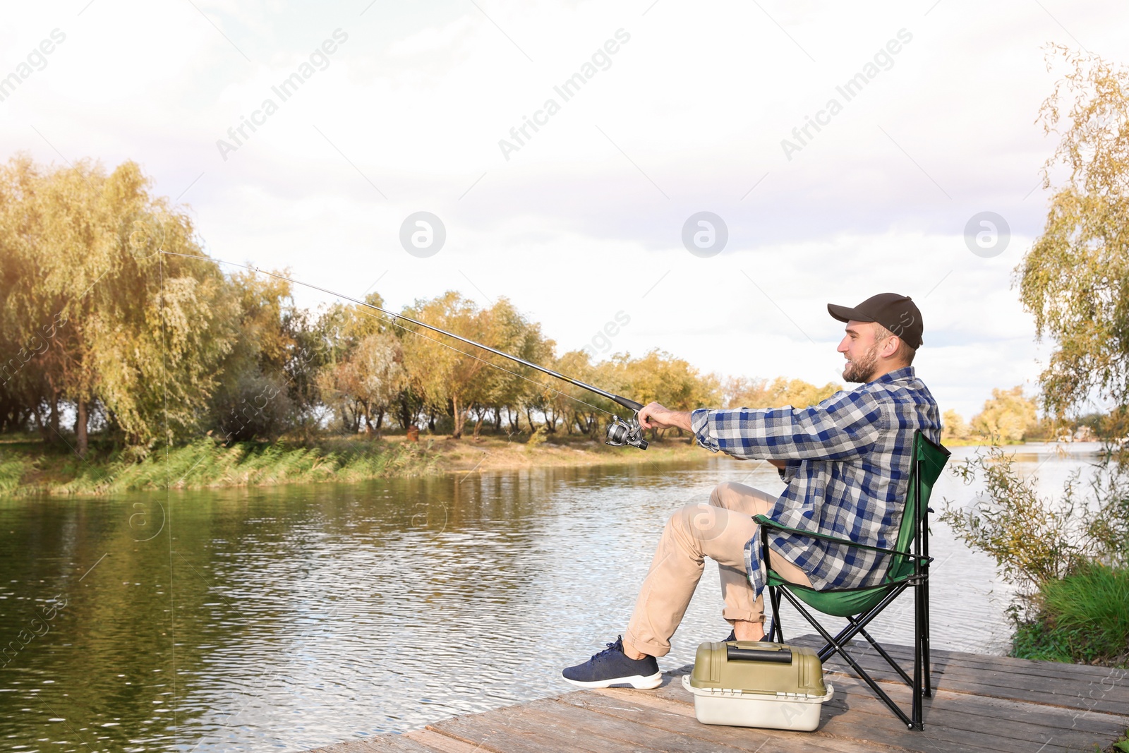 Photo of Man with rod fishing on wooden pier at riverside. Recreational activity