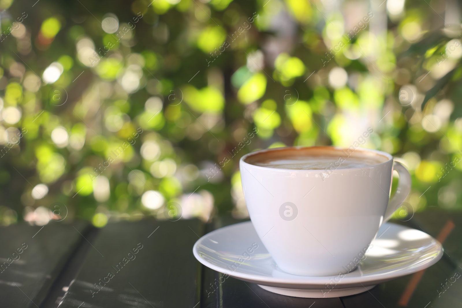 Photo of Cup of aromatic coffee with foam on table in outdoor cafe. Space for text