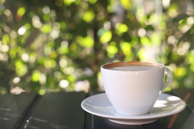 Cup of aromatic coffee with foam on table in outdoor cafe. Space for text