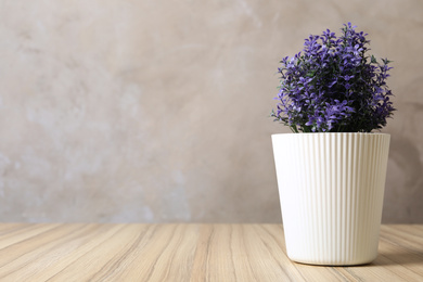 Photo of Beautiful artificial plant in flower pot on wooden table against grey background. Space for text