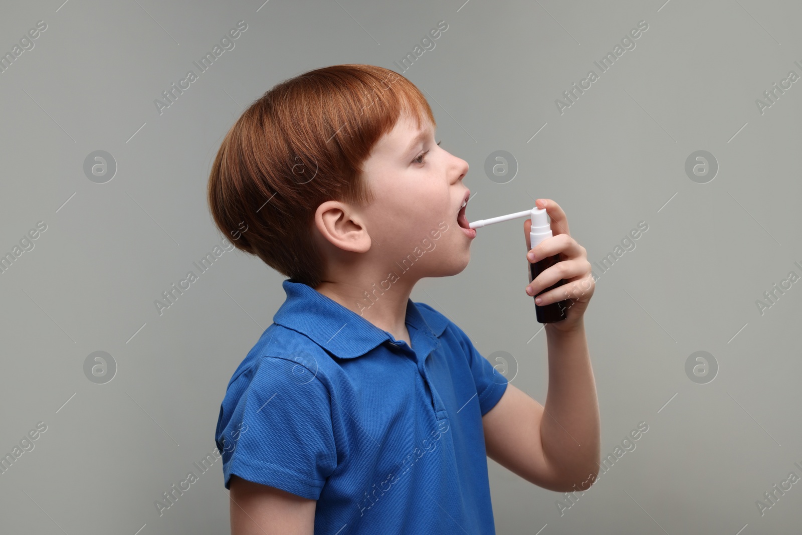 Photo of Little boy using throat spray on grey background