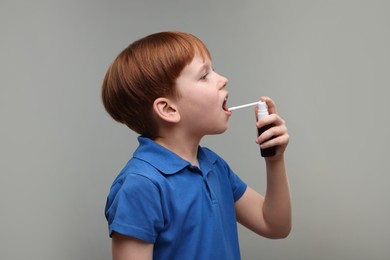Little boy using throat spray on grey background