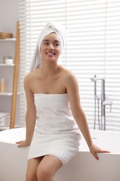 Photo of Smiling young woman near tub after shower in bathroom