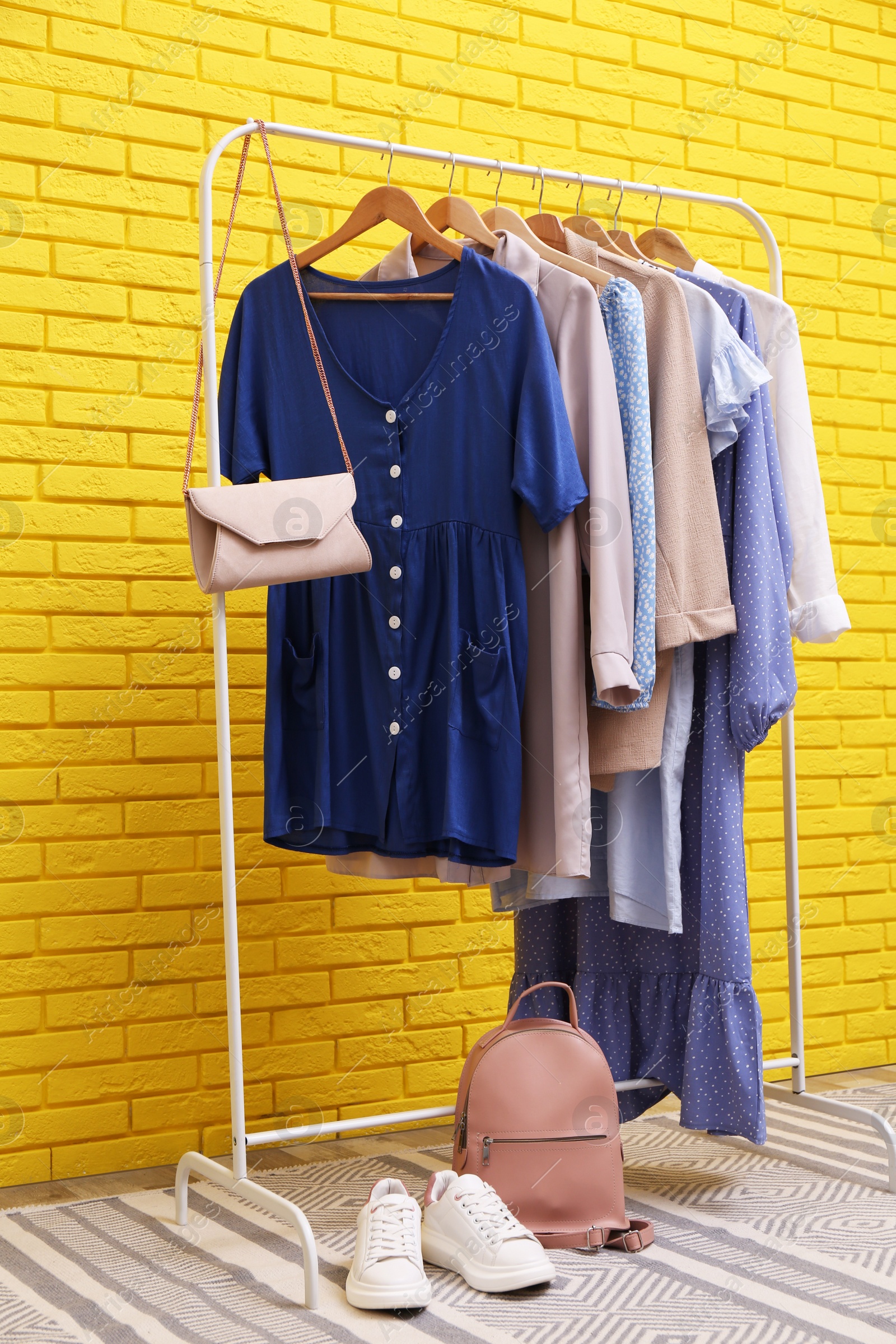 Photo of Rack with different stylish clothes near yellow brick wall in room