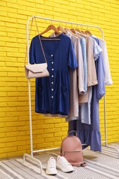 Rack with different stylish clothes near yellow brick wall in room