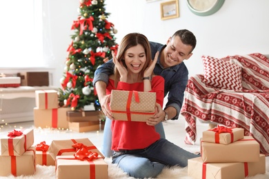 Photo of Young man surprising his girlfriend with Christmas gift at home