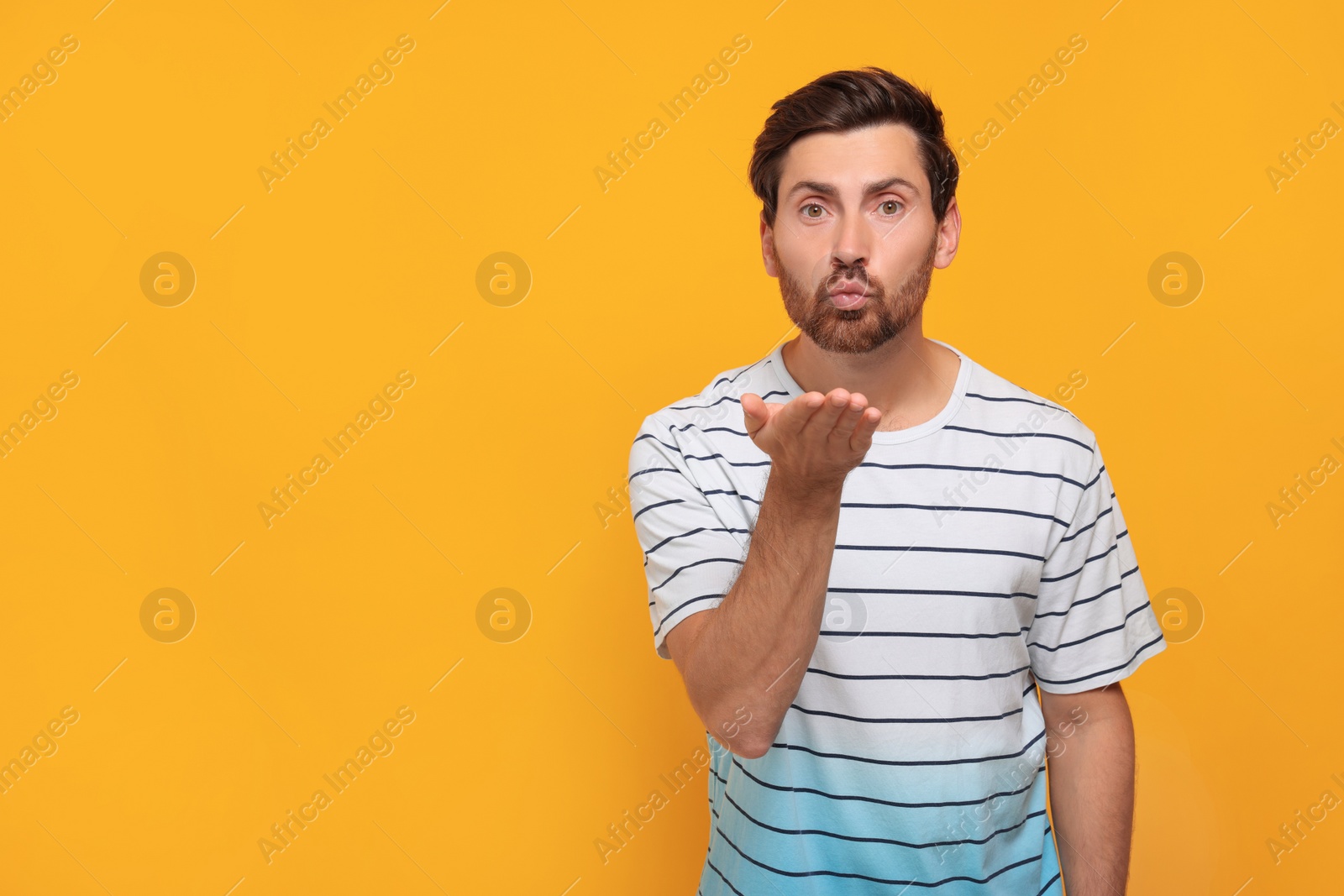 Photo of Handsome man blowing kiss on orange background. Space for text