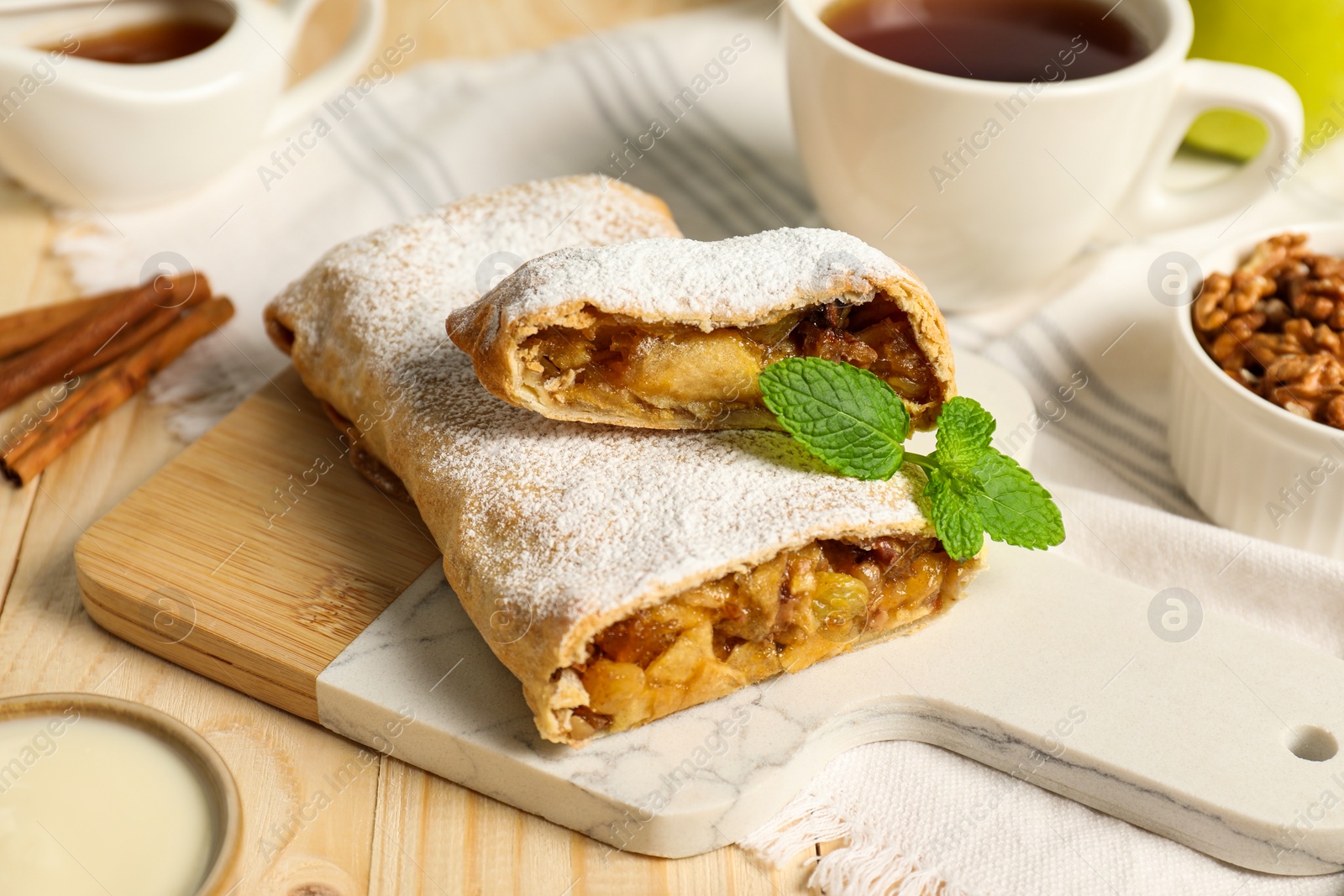 Photo of Delicious strudel with apples, nuts and raisins on wooden table, closeup