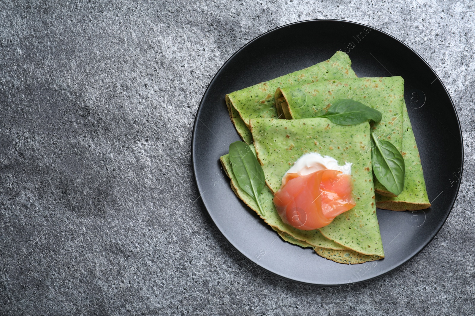 Photo of Delicious spinach crepes with salmon and cream on grey table, top view. Space for text