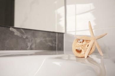 Photo of Natural loofah sponge and starfish on washbasin in bathroom, space for text