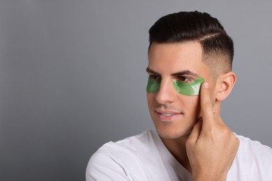 Man applying green under eye patch on grey background. Space for text