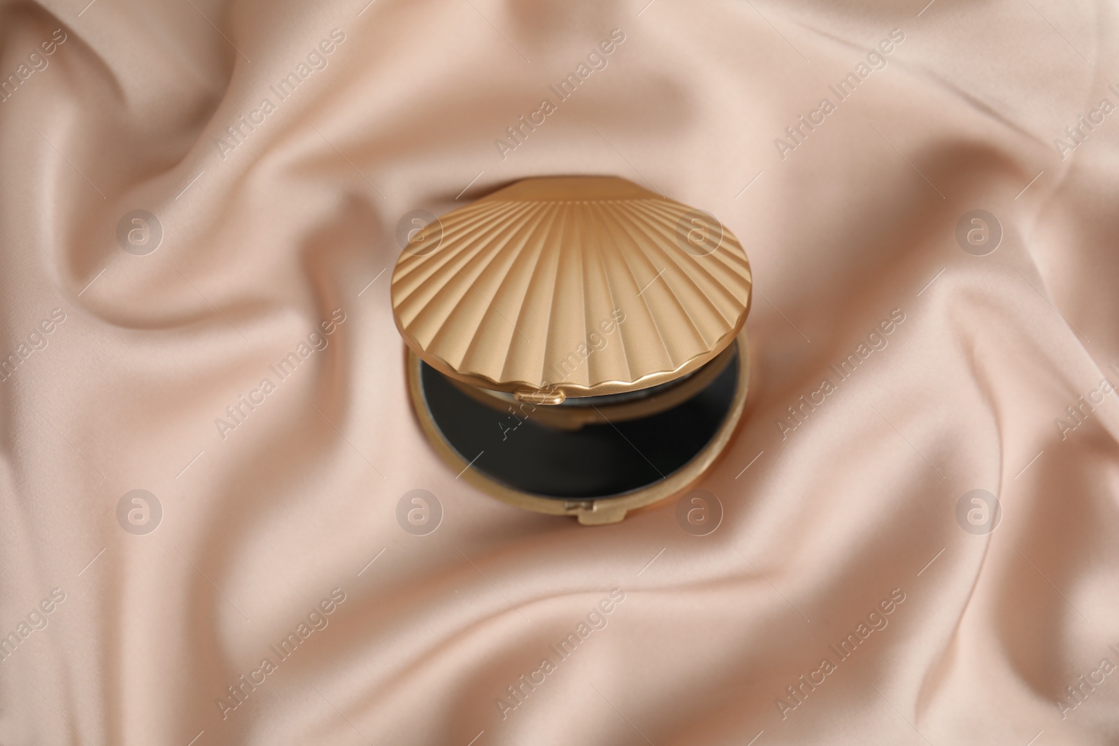 Photo of Bright cosmetic pocket mirror on rose gold fabric, top view