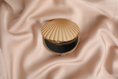 Bright cosmetic pocket mirror on rose gold fabric, top view