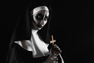 Photo of Scary devilish nun with cross on black background, space for text. Halloween party look