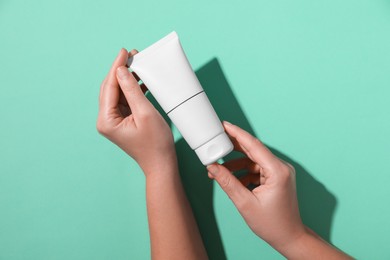 Woman with tube of hand cream on turquoise background, top view