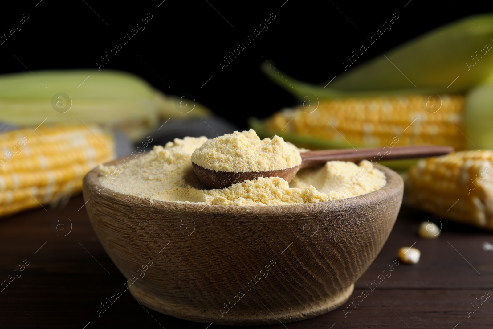 Photo of Corn flour in bowl and fresh cobs on wooden table