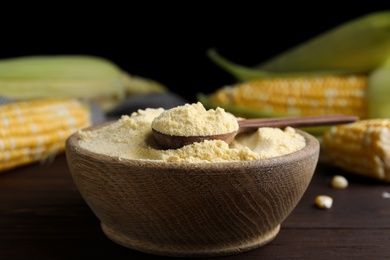 Photo of Corn flour in bowl and fresh cobs on wooden table