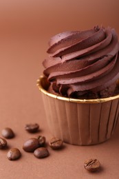 Delicious chocolate cupcake and coffee beans on brown background, closeup