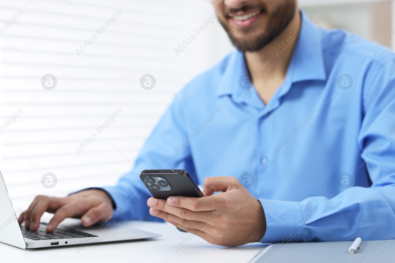 Photo of Man using smartphone while working with laptop at white table in office, closeup