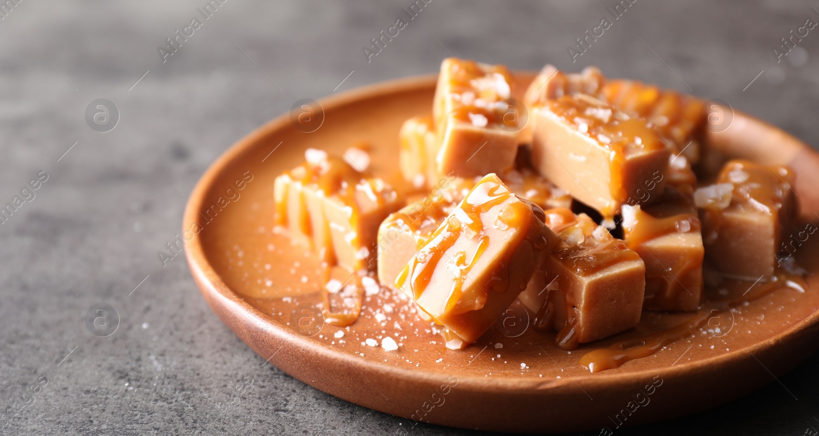 Photo of Plate with tasty candies, caramel sauce and salt on grey table, closeup