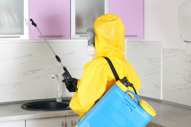 Pest control worker spraying pesticide in kitchen