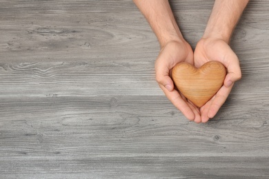 Photo of Young man holding heart on grey wooden background, top view with space for text. Donation concept